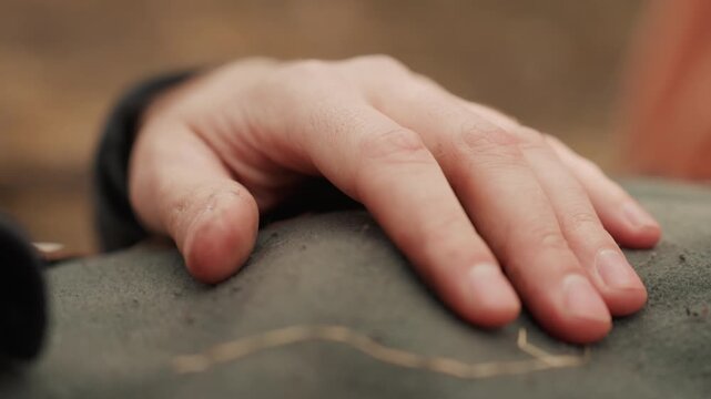 Close view shows child hand resting softly on coarse canvas or upholstery fabric beside visible stitching and seam, with curled fingers, warm light, tactile texture, gentle pressure, and calm