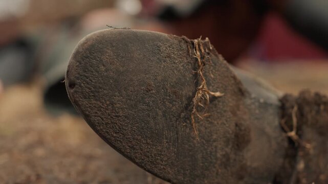 Low-angle close-up shows worn boot toe pressing into rough ground, with heavy scuff marks, lifted frayed stitching, dusty leather, and shallow depth of field for gritty tactile detail