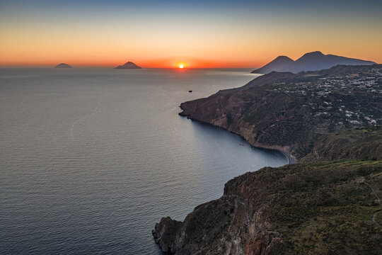 Aerial view of the sunset over the rugged coastline of Lipari with calm sea and distant volcanic islands in the Aeolian archipelago, Lipari, Sicily, Italy.