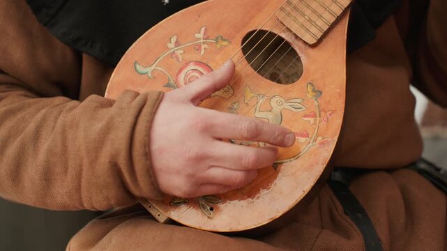 person strumming or plucking strings of a wooden musical instrument in an indoor setting, close-up of hands and torso, brown clothing, strings, music lessons, practice, performance, natural.