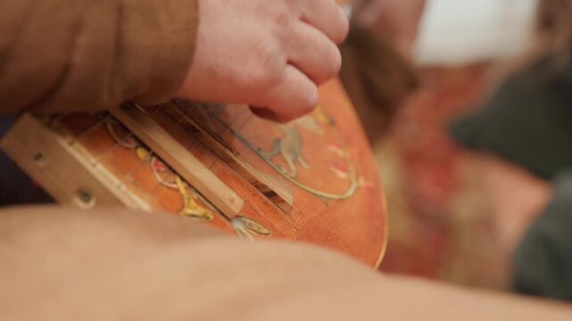 Detailed close-up of hands actively playing aged acoustic guitar, right hand plucking near soundhole while left hand shifts chords on fretboard, with warm indoor light and subtle finger motion