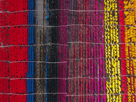 Aerial view of long strips of vibrant colorful fabrics hanging to dry on lines in a textile dyeing area in Narayanganj, Dhaka, Bangladesh.