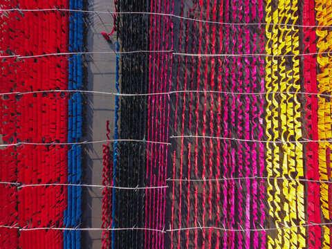 Aerial view of vibrant colorful fabrics hanging to dry on bamboo poles over water in Narayanganj, Dhaka, Bangladesh.
