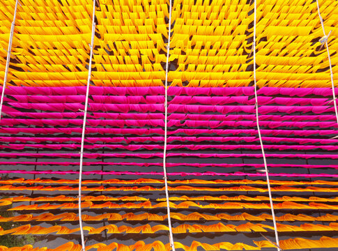 Aerial view of vibrant yellow, pink, and orange fabrics hanging to dry in rows over water in Narayanganj, Dhaka, Bangladesh.
