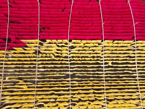 Aerial view of vibrant red and yellow fabrics hanging on bamboo frames to dry over water in Narayanganj, Dhaka, Bangladesh.
