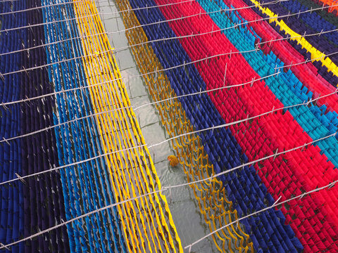 Aerial view of vibrant colorful fabrics hanging to dry on wooden racks over water in a textile dyeing area in Narayanganj, Dhaka, Bangladesh.