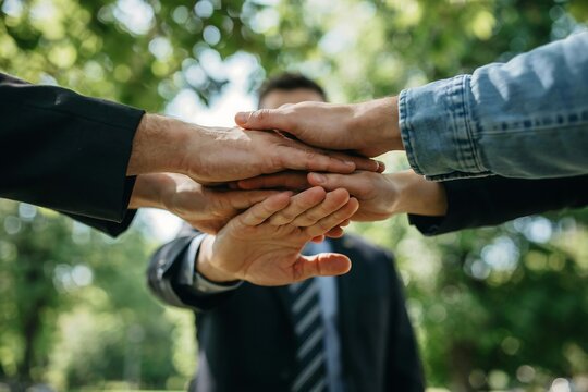Close-up of diverse hands stacking together in unity outdoors with blurred green trees