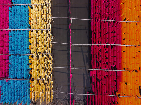 Aerial view of colorful fabrics hanging to dry in long rows, creating a vibrant pattern of blue, yellow, pink, and orange textiles in the textile industry, Narayanganj, Dhaka, Bangladesh.