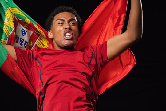 Man shouting and celebrating while wearing red athletic shirt with Portuguese flag at stadium