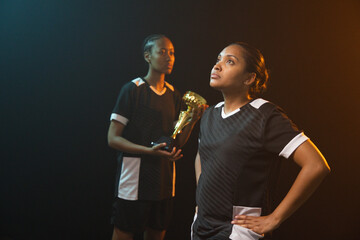 Fototapeta premium African American female teammates posing in studio wearing black-white jerseys and gold boot trophy