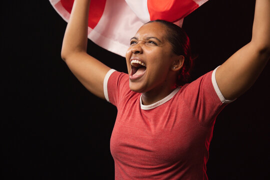African woman shouting while holding red-and-white flag above head in studio wearing red ringer tee