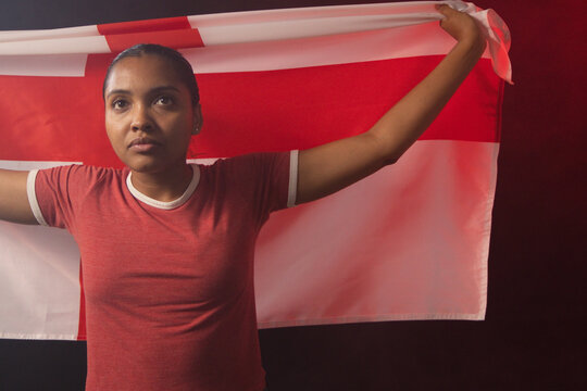 African American woman holding red-and-white flag behind shoulders in studio wearing ringer T-shirt