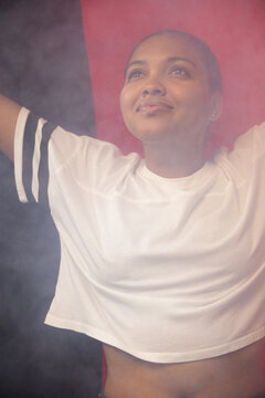 African American woman standing arms raised in studio wearing white cropped tee, black stripes, fog
