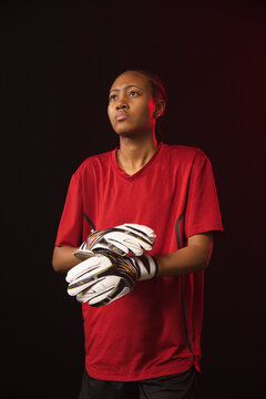 African American female standing in studio wearing red jersey holding white goalkeeper gloves