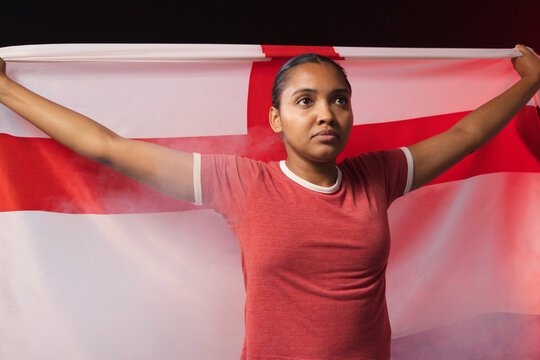 Woman standing in studio with arms extended holding white flag with red cross in red T-shirt