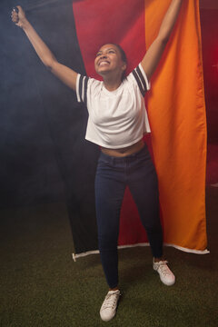 African American woman standing in studio on turf, holding orange panel and phone, smiling upward