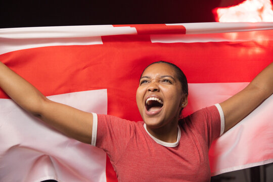 Adult African woman holding red-and-white-flag in red-tee-white-trim, cheering at arena spotlight