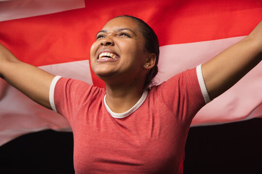 African woman raising arms smiling and looking upward at studio with red t-shirt flag stud earring