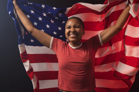 African American woman standing holding US flag in studio wearing red T-shirt and denim