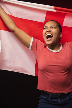 Adult African woman holding red flag with white cross, wearing red T-shirt, shouting in studio