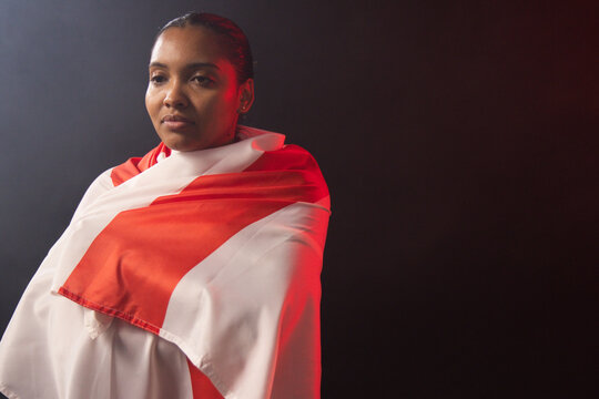 African woman standing and posing in studio, wearing red-and-white draped fabric and stud earring