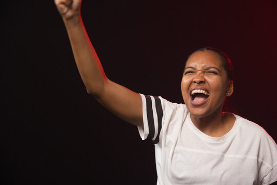 African American woman raising right arm, shouting in studio in white tee with stripes, copy space
