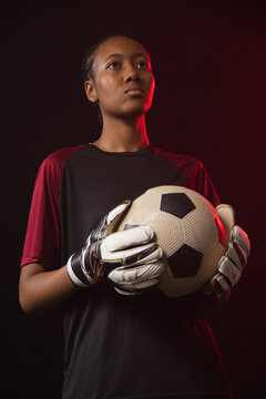 African woman goalkeeper holding classic soccer ball in jersey and goalkeeper gloves in studio