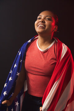 Adult African American woman posing, draping American flag, wearing red crewneck with studio lights