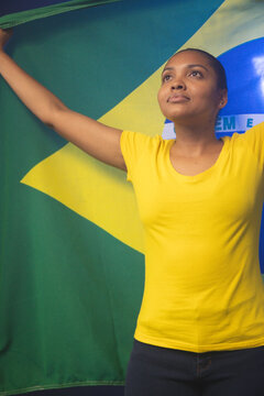 African American woman holding Brazilian flag, wearing yellow t-shirt and dark pants in studio