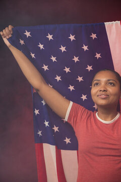African American woman holding large American flag, wearing red ringer tee in studio, copy space
