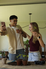Couple taking selfie while potting seedlings at wooden table with smartphone and trowel © wavebreak3