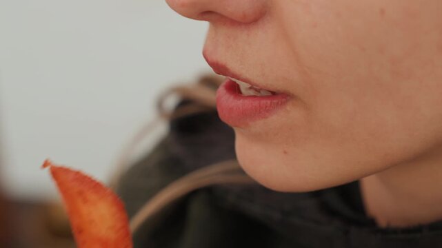 Close-up view of lower face from nose to neck capturing eating action with lips parting, tongue and teeth meeting seasoned fried snack, hand bringing crisp bite toward mouth in soft diffused light