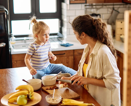 Portrait of a mother and daughter preparing and eating breakfast and having fun in the kitchen at home