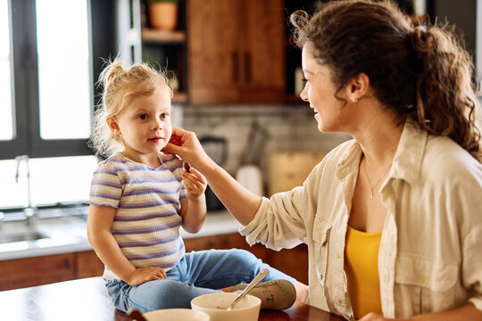 Portrait of a mother and daughter preparing and eating breakfast and having fun in the kitchen at home
