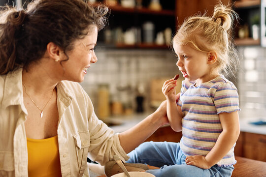 Portrait of a mother and daughter preparing and eating breakfast and having fun in the kitchen at home