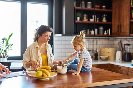 Portrait of a mother and daughter preparing and eating breakfast and having fun in the kitchen at home