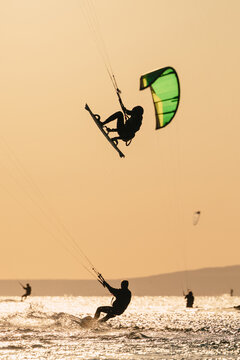 Kite boarder performing a high jump over the sea against a warm sunset