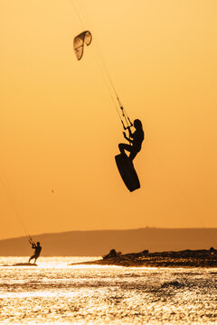 Kitesurfer jumping high above sea with kite against a golden sky