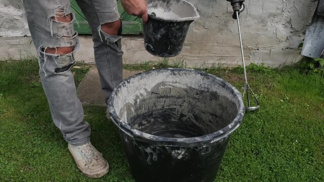 Worker Pouring Dry Plaster Into a Bucket of Water Outdoors
