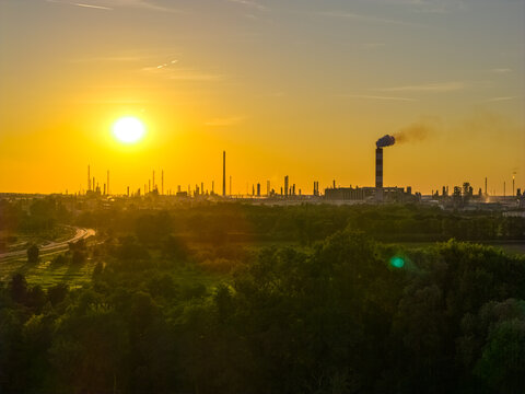 Aerial view of the PKN Orlen refinery complex at sunset with industrial chimneys, smoke, and lush green trees in the foreground in Plock, Masovian Voivodeship, Poland.