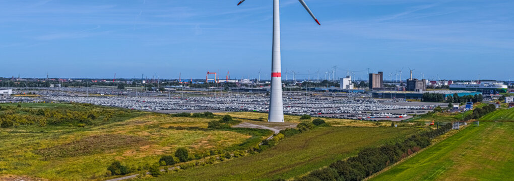 Aerial view of Volkswagenwerk Emden with a large parking lot filled with new cars, a wind turbine in the foreground, and industrial facilities in Emden, Niedersachsen, Germany.