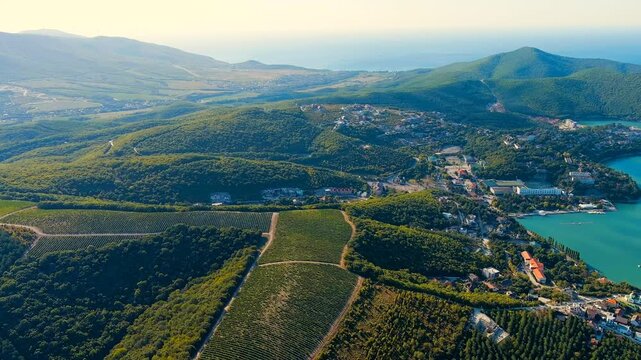 Abrau-Diurso, Krasnodar Krai, Russia. Lake Abrau. Embankment and village. Summer. Fields with vineyards on the hills. Drone footage