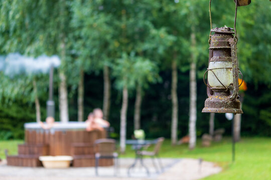 Rusty vintage hurricane lantern hanging in focus with an outdoor wooden hot tub blurred in the background