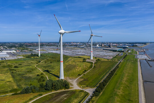 Aerial view of the Volkswagenwerk Emden car factory with wind turbines, large parking lots filled with vehicles, and green fields near the river in Emden, Niedersachsen, Germany.