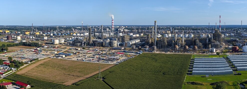 Aerial view of the PKN Orlen refinery complex in Plock, featuring industrial towers, storage tanks, and smoking chimneys surrounded by fields. Plock, Masovian Voivodeship, Poland.