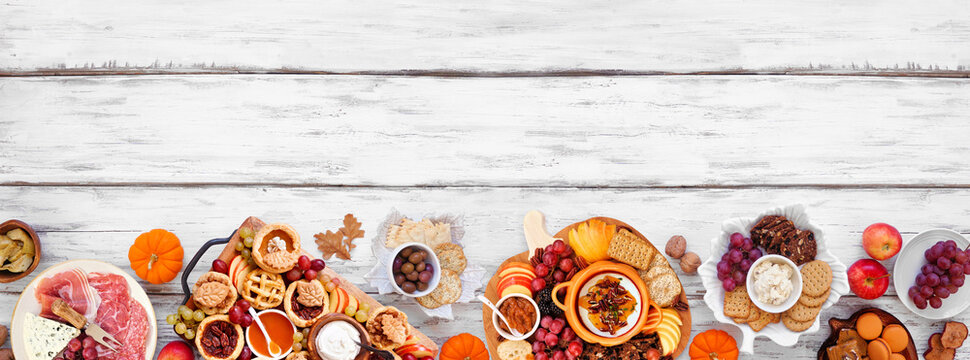 Fall or Thanksgiving appetizers, sweets and grazing boards. Top down view bottom border on a white wood banner background. Pumpkin and apple snacks, charcuterie, pies, desserts.