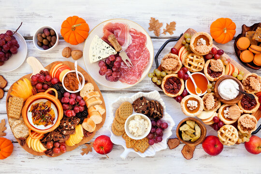 Fall or Thanksgiving appetizers, sweets and grazing boards. Overhead view table scene on a white wood background. Pumpkin and apple snacks, charcuterie, pies, desserts.
