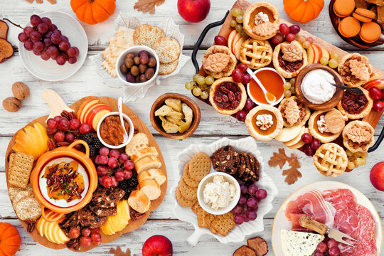 Autumn or Thanksgiving appetizers, sweets and grazing boards. Top down view table scene on a white wood background. Pumpkin and apple snacks, charcuterie, pies, desserts.