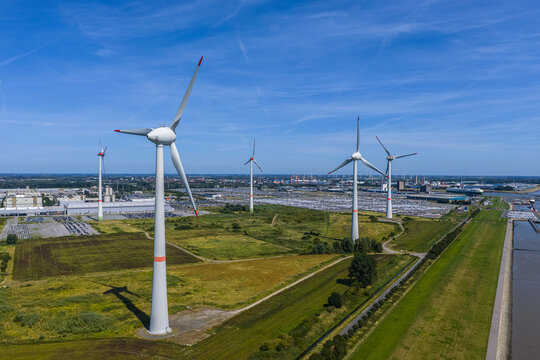 Aerial view of Volkswagenwerk Emden with wind turbines in the foreground and the industrial factory complex in the background under a clear blue sky in Emden, Niedersachsen, Germany.