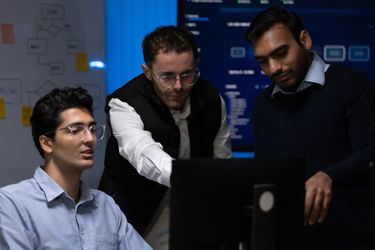 Indian and Caucasian male coworkers discuss work on a computer screen in a technology office, collaborating on software workflow, planning, and problem solving